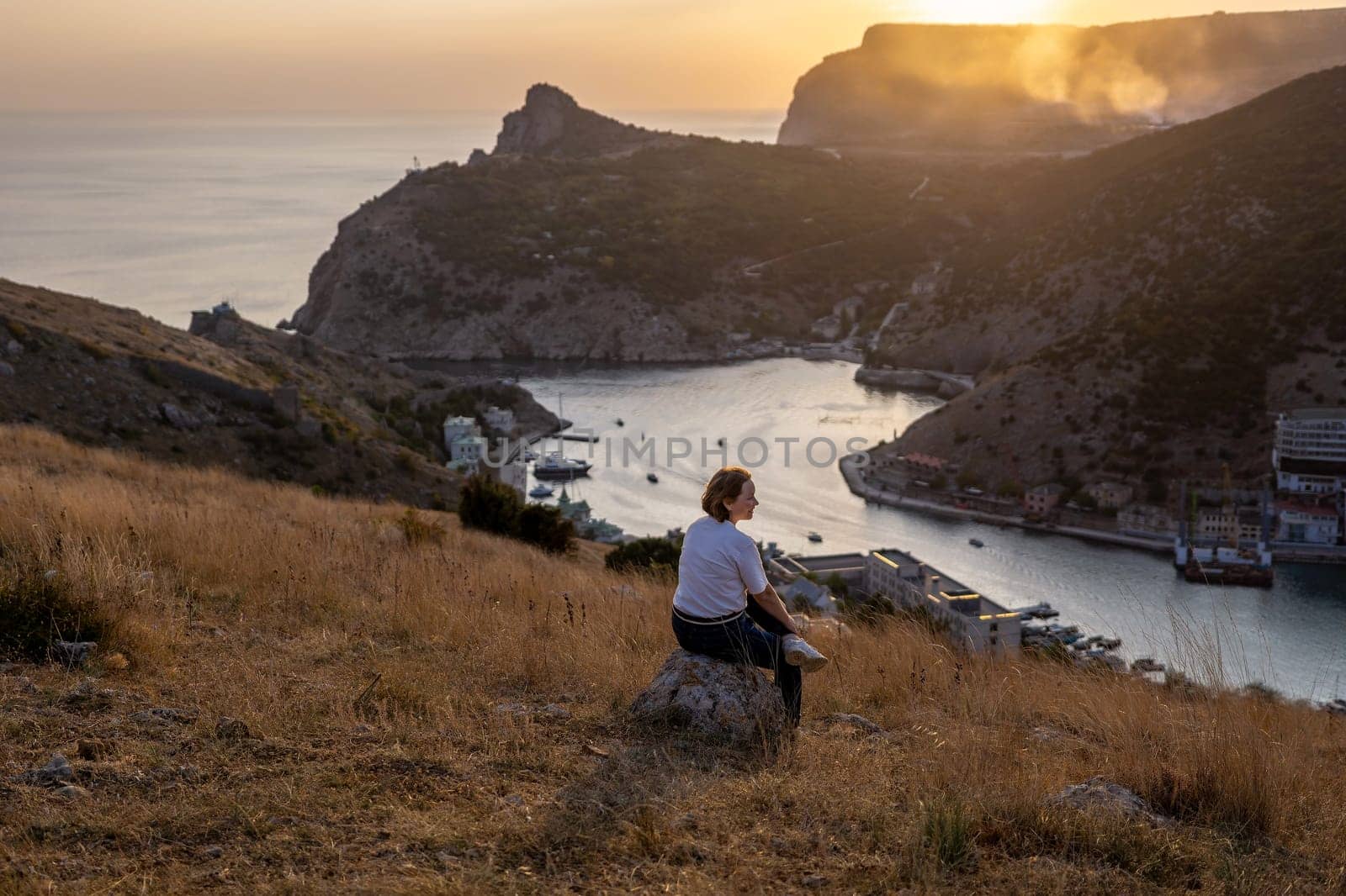 Happy woman on sunset in mountains. Woman siting with her back on the sunset in nature in summer. Silhouette. by Matiunina