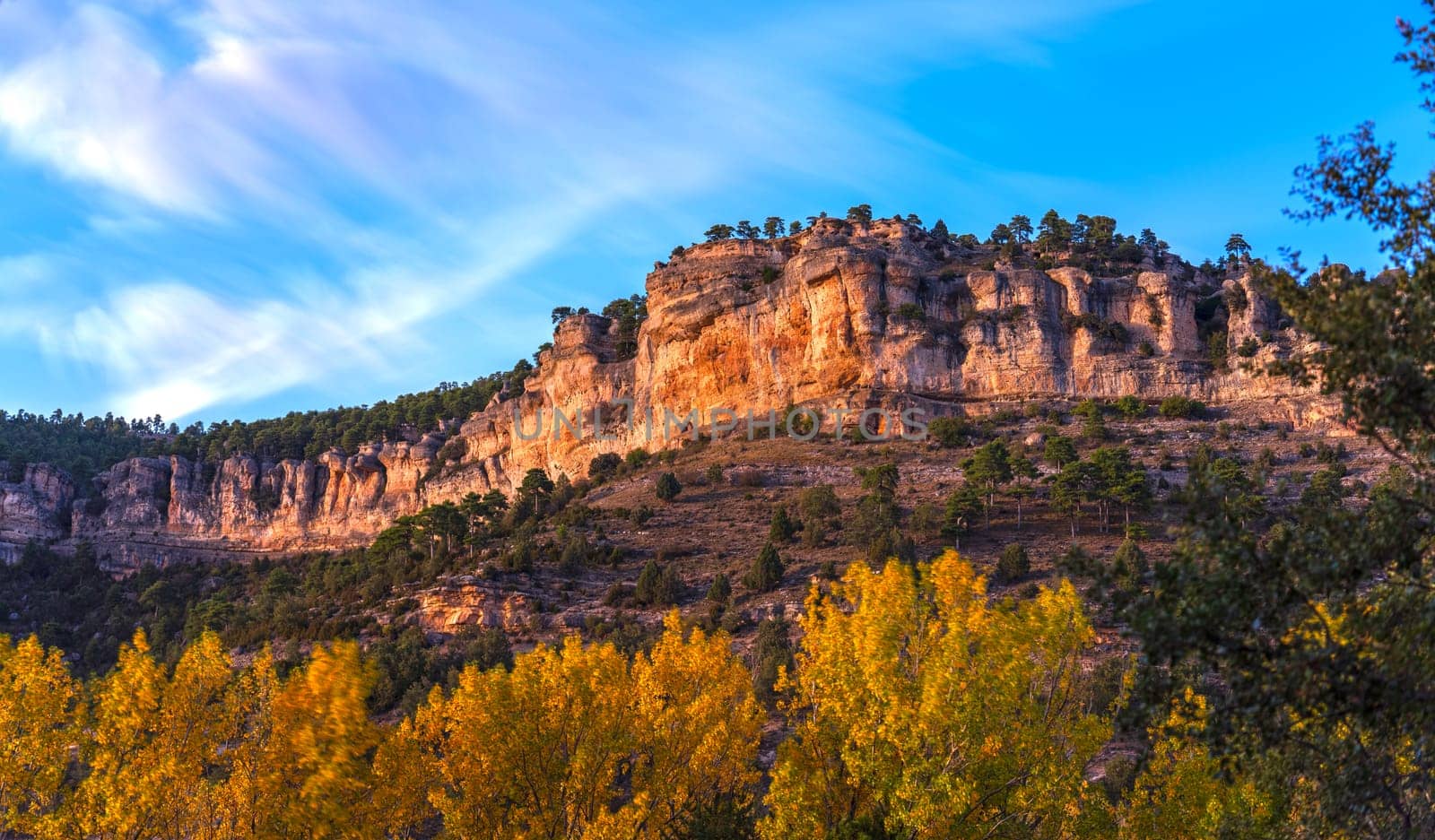 Autumn trees and a cliff under a twilight blue sky.