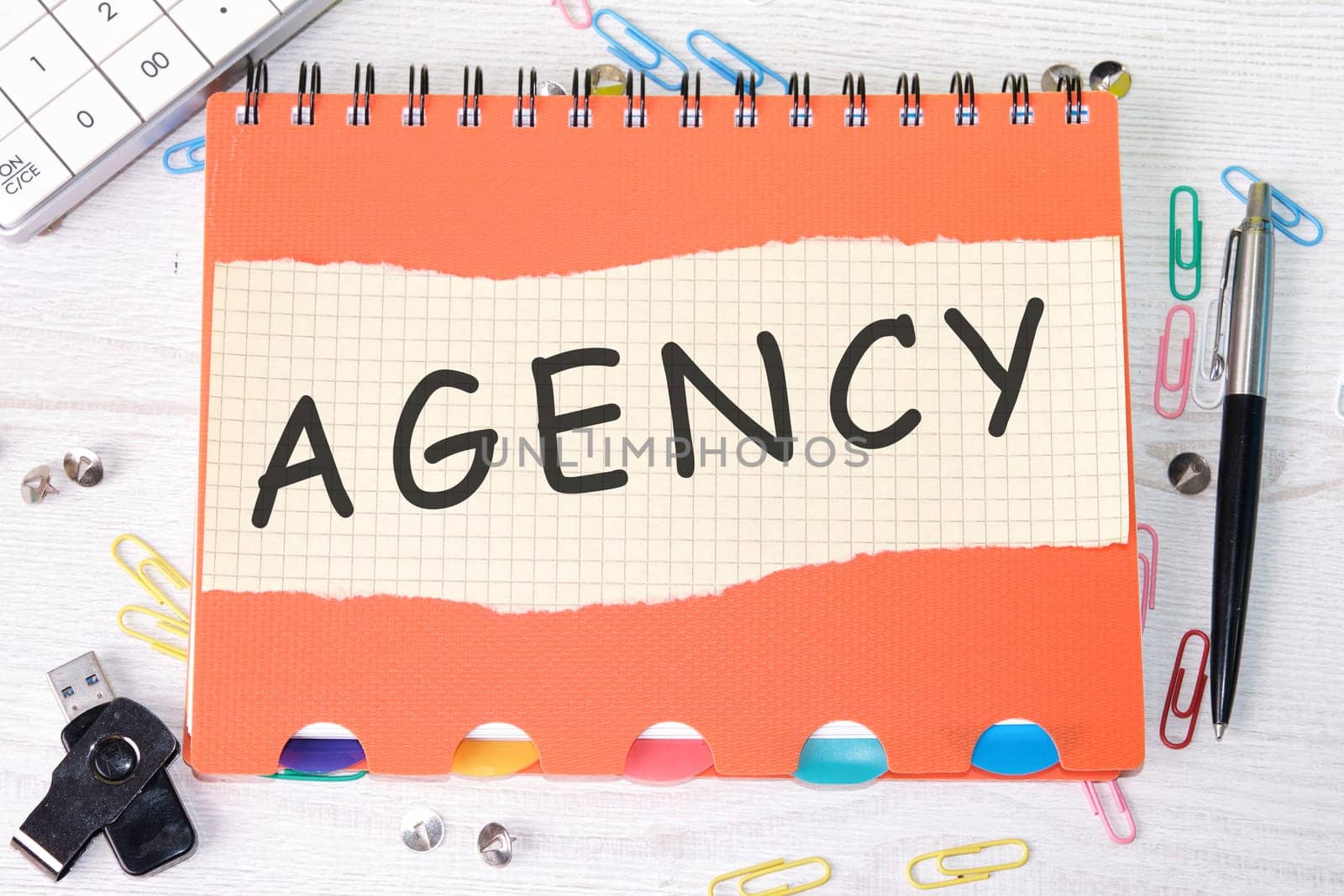 Agency word is written on a sheet in a cage lying on a notebook on the table next to stationery