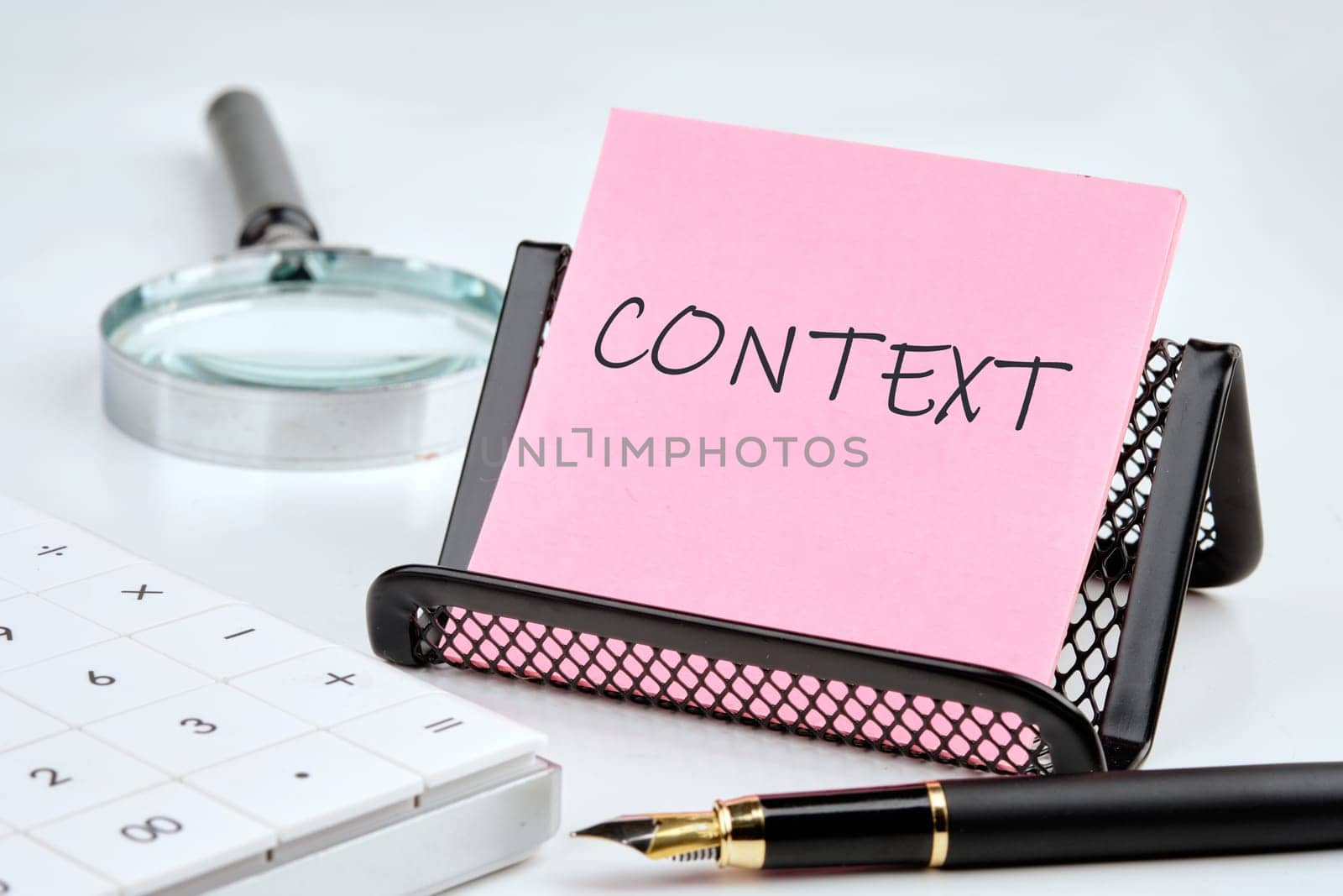 CONTEXT word on the sticker on the stand on a white background next to a fountain pen, calculator and magnifying glass on a white background