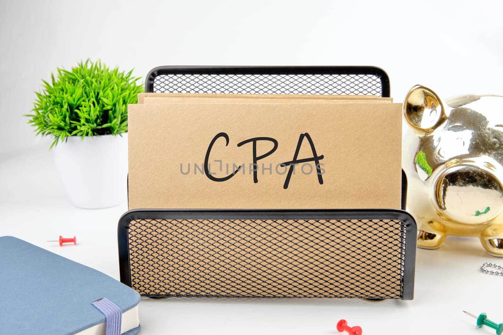CPA, Certified Public Accountant or Cost per Action text on paper next to piggy bank, notepad, flower on a white background