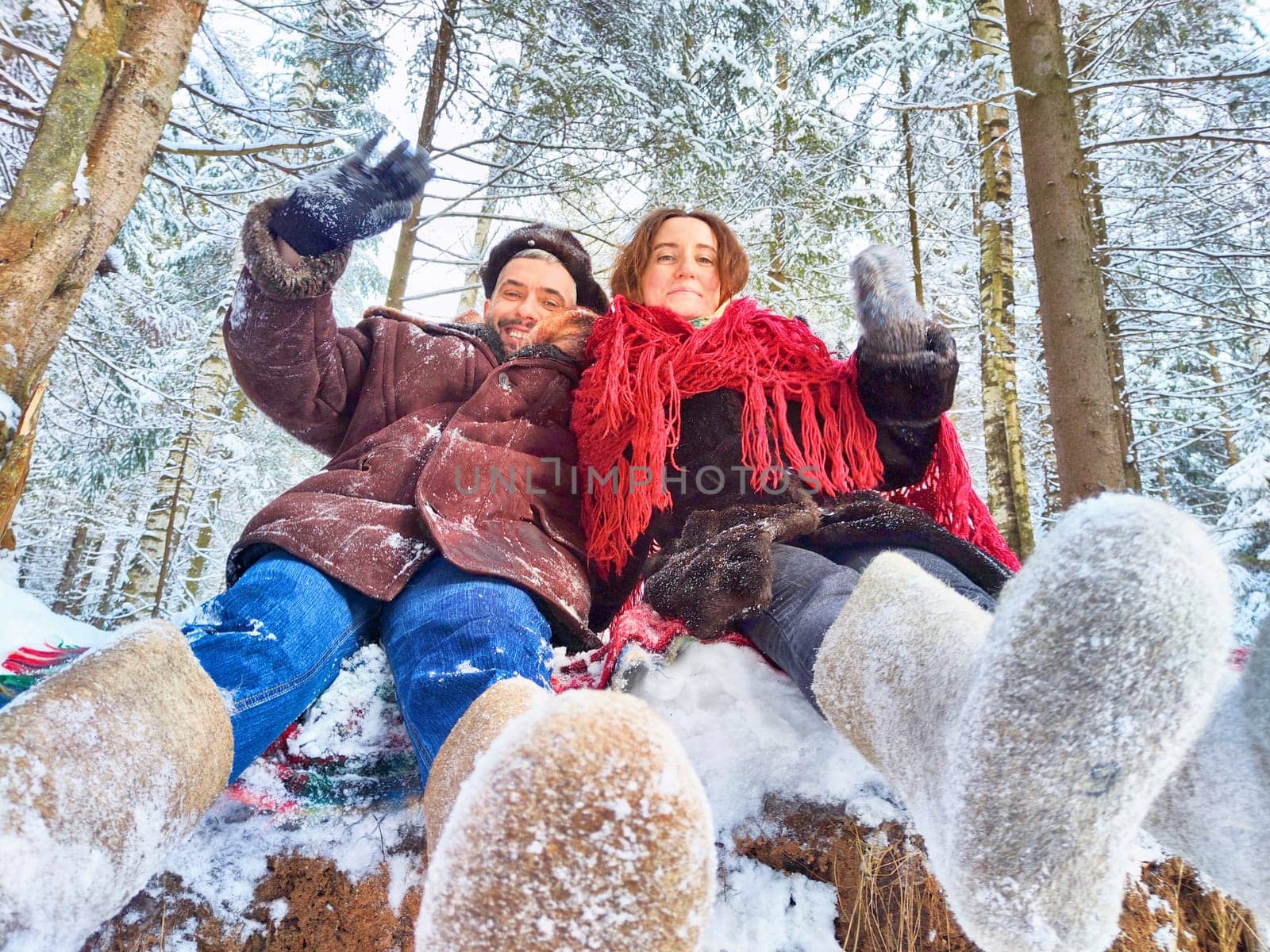 A cute middle-aged couple hugging in a snowy forest in winter. Photo shoot in stylized clothes of the USSR. Hat with earflaps, felt boots by keleny