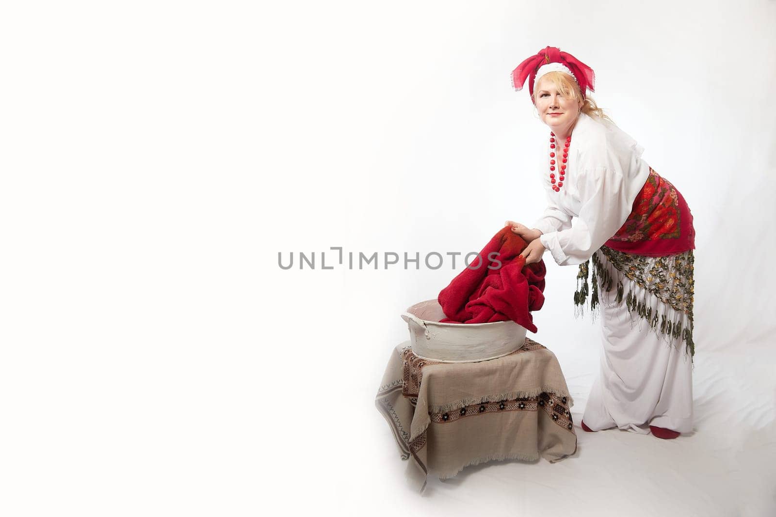 Portrait of heerful funny adult mature woman solokha washing clothes in basin. Female model in national ethnic Slavic style. Stylized Ukrainian, Belarusian or Russian woman in comic photo shoot