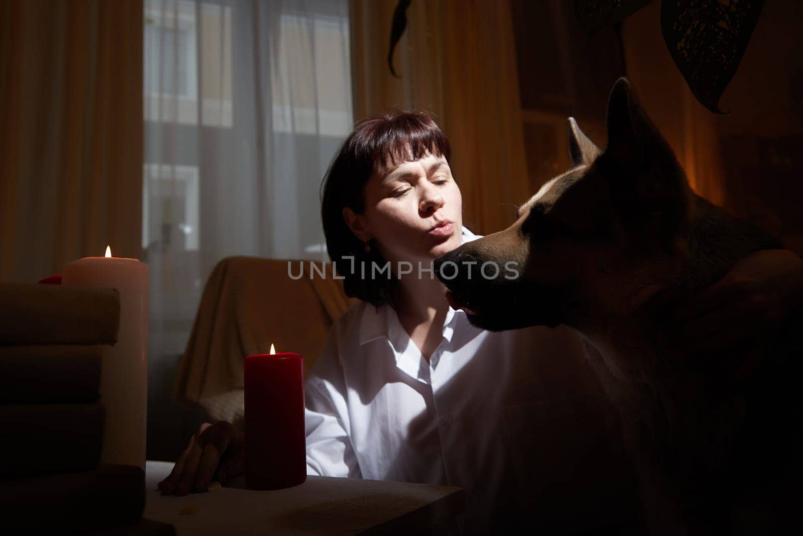 Adult mature woman with big shepherd dog in white shirt in dark room. Concept of loneliness and love for animals and pets by keleny