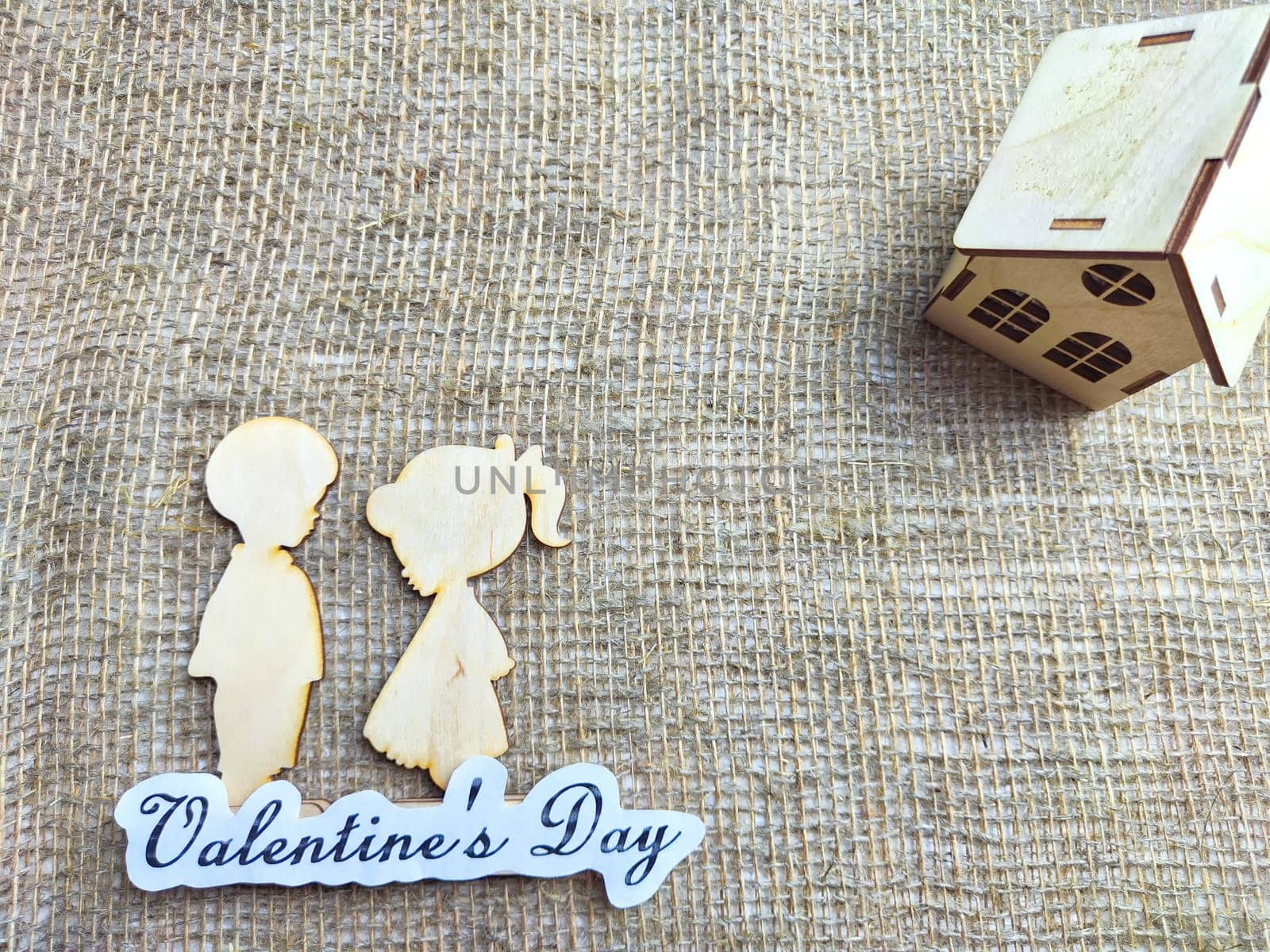 Wooden figurines of a couple, a house and the inscription Valentine's Day. The concept of a holiday of love and lovers. Background, texture, place for text and copy space