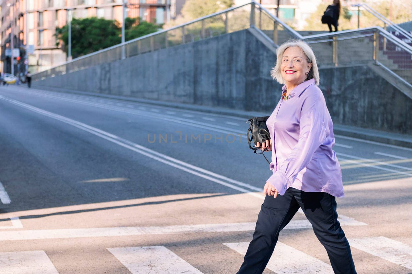senior woman smiling happy crossing a city street by pedestrian crossing, concept of elderly people leisure and active lifestyle, copy space for text