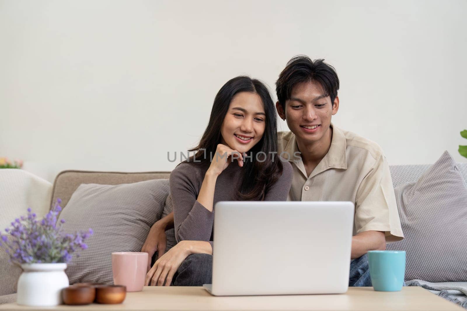 Young couple asian using laptop together while sitting on sofa at home by nateemee