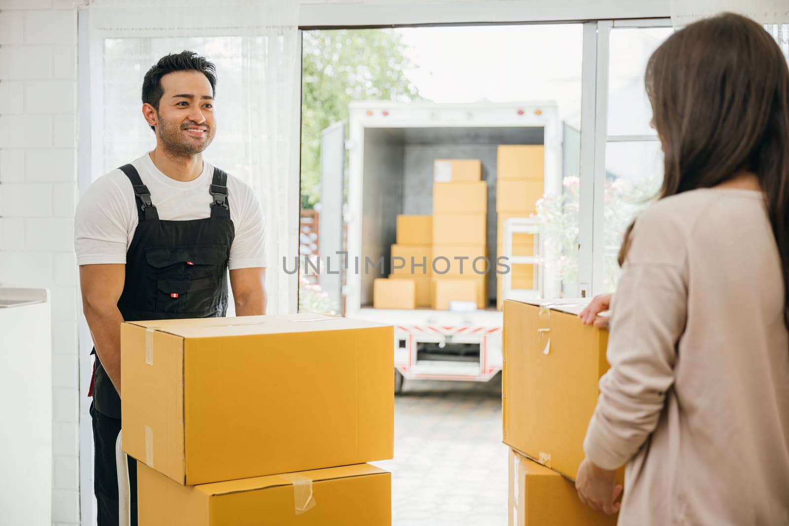 Couple receives expert moving service inside their home. Uniformed movers unload boxes from truck ensuring customer satisfaction. Professional service and teamwork are evident. Moving new house