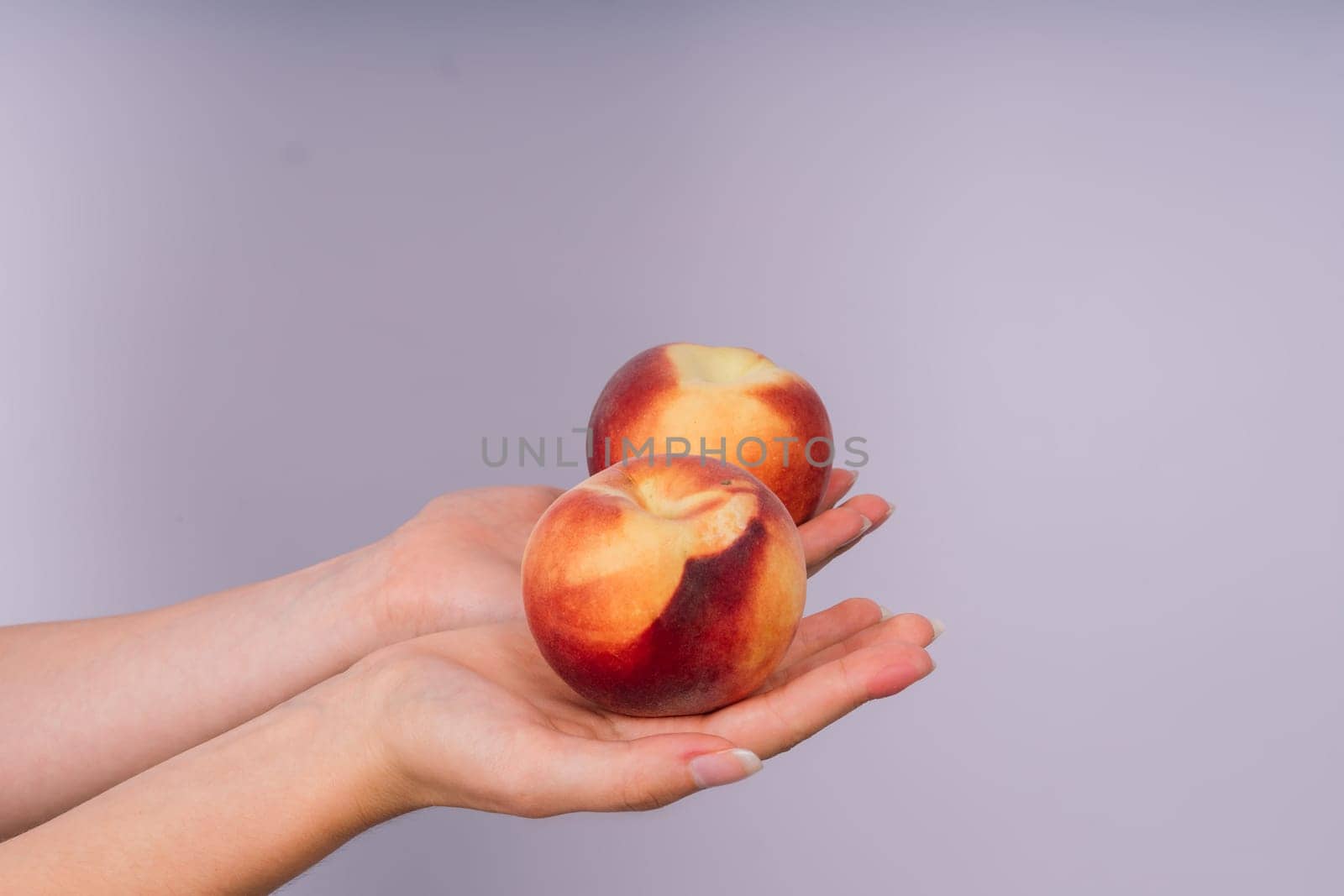 Studio portrait of a happy young woman, smiling, holding ripe nectarines in hands