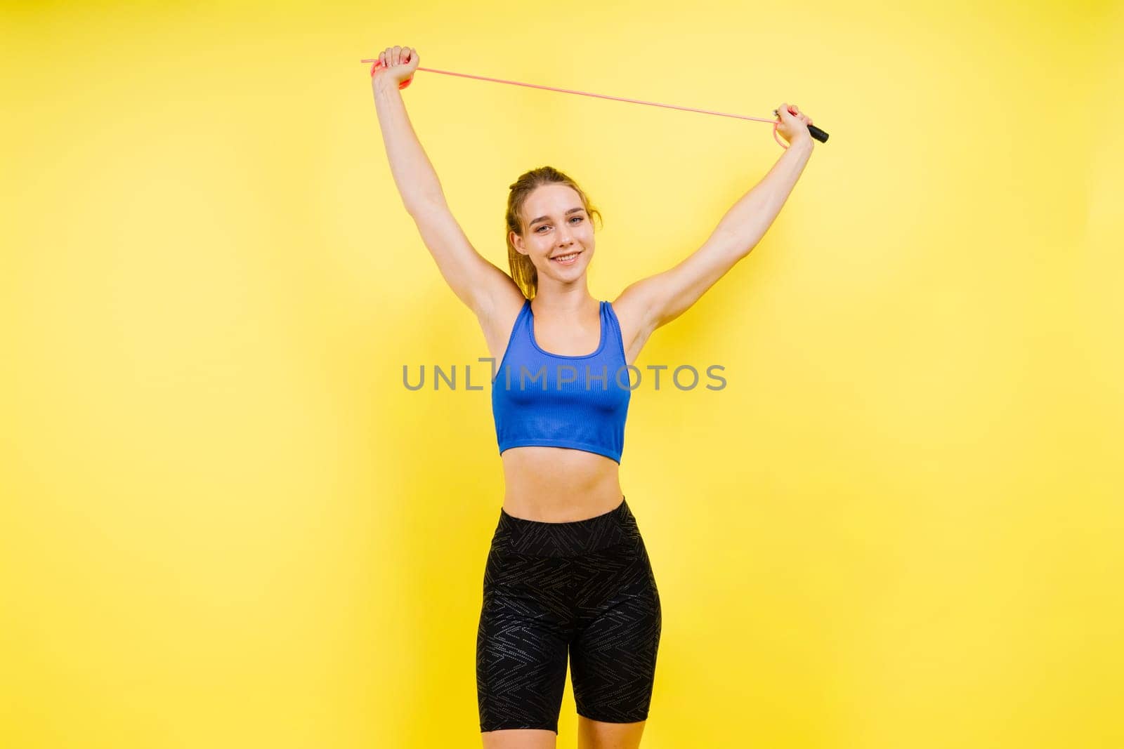 Fit female athlete with jumping with rope during fitness training against yellow background