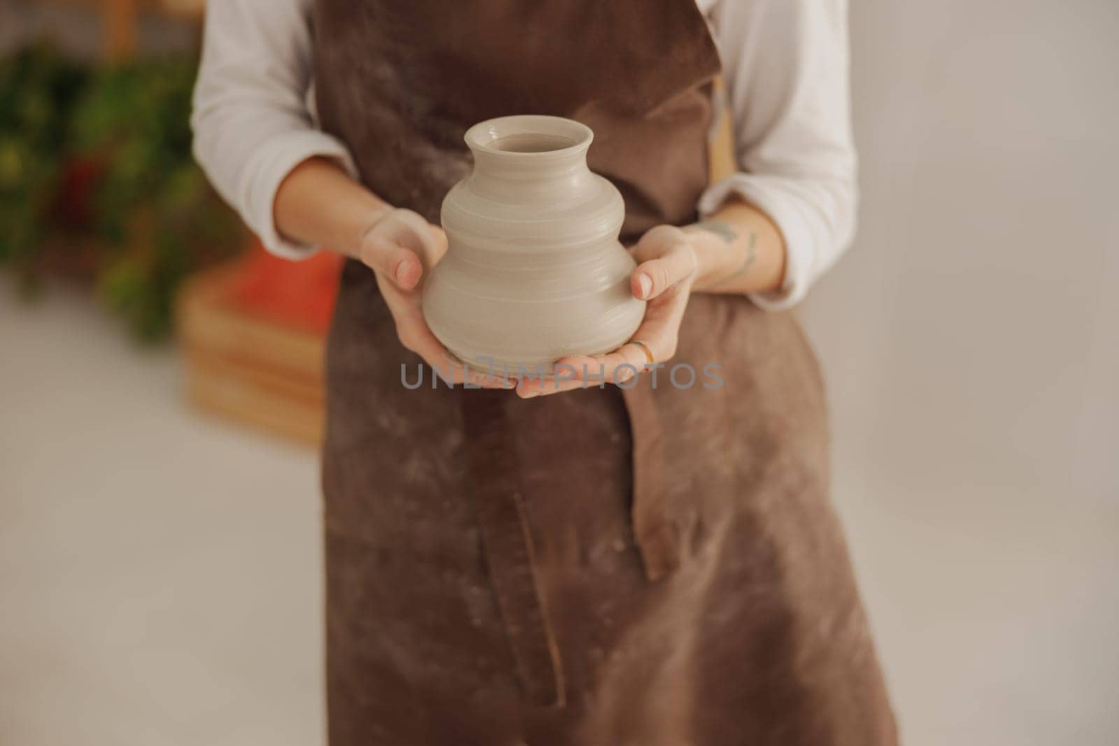 Close up of potter holding unfired clay vase while standing in pottery studio. High quality photo