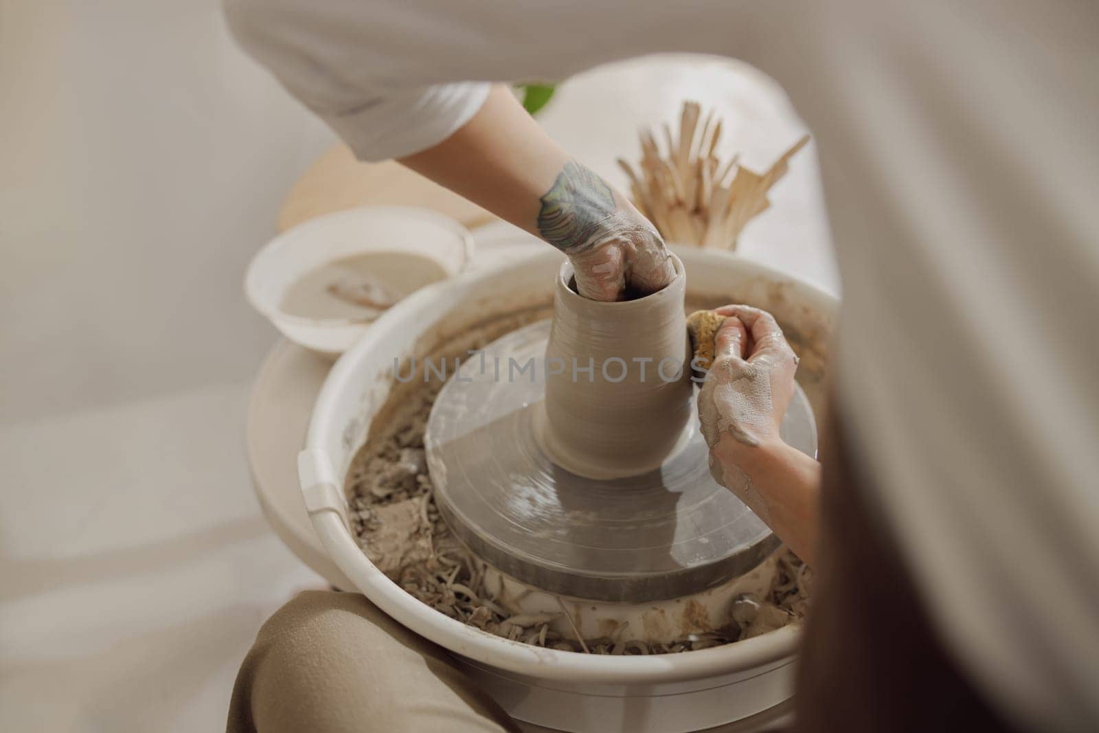 Female potter in apron making shape of clay vase on spinning pottery tool in ceramic workshop by Yaroslav_astakhov