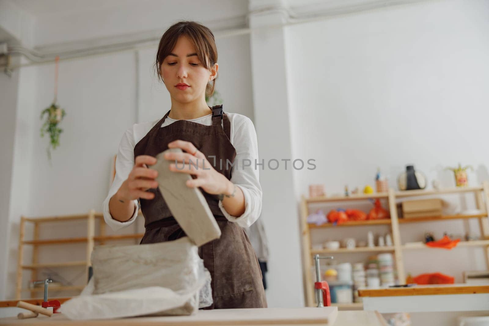 Focused ceramist woman wearing apron is preparing clay to make pottery pieces in her studio by Yaroslav_astakhov