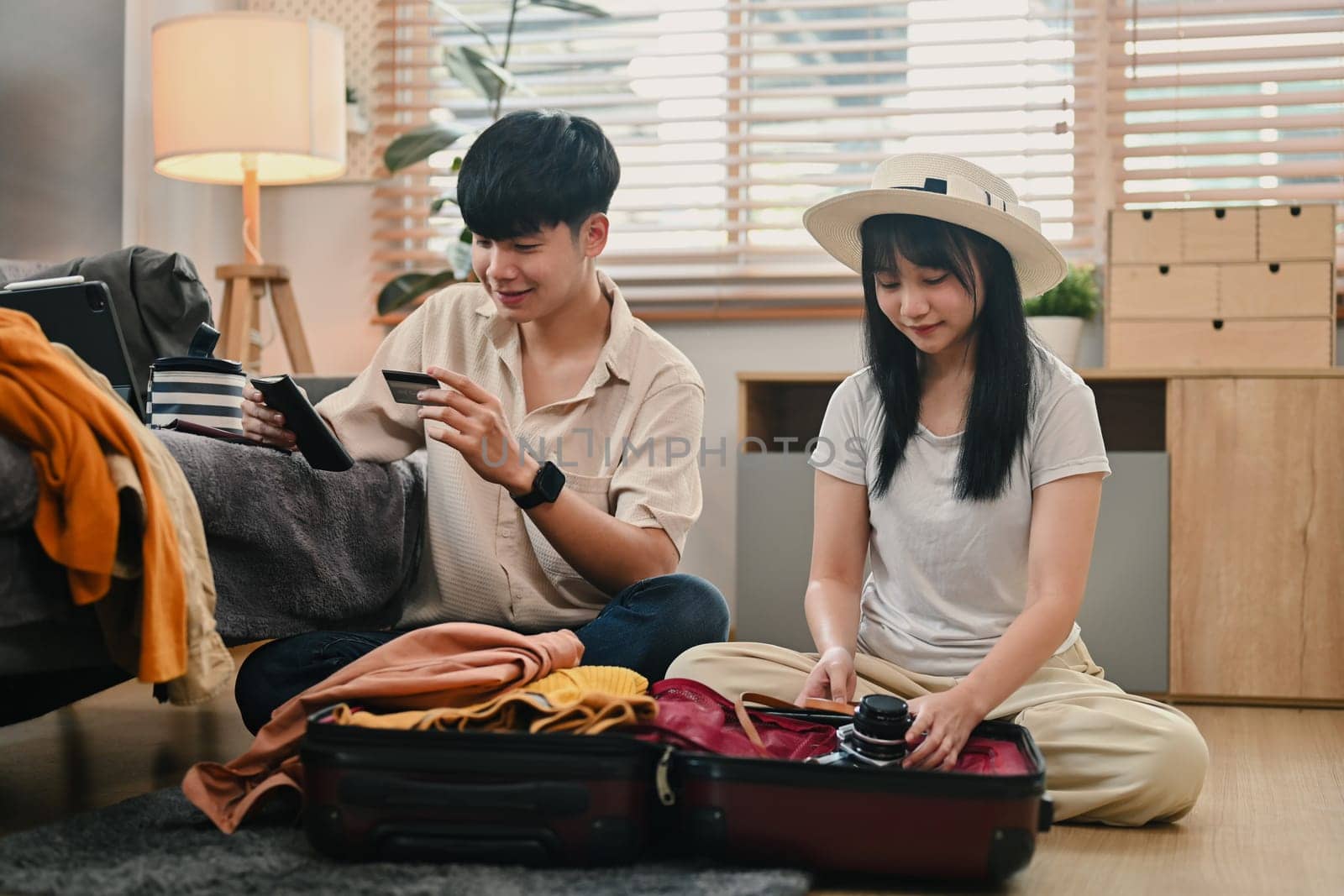 Happy young couple packing clothes into travel bag, getting ready for their holiday trip.