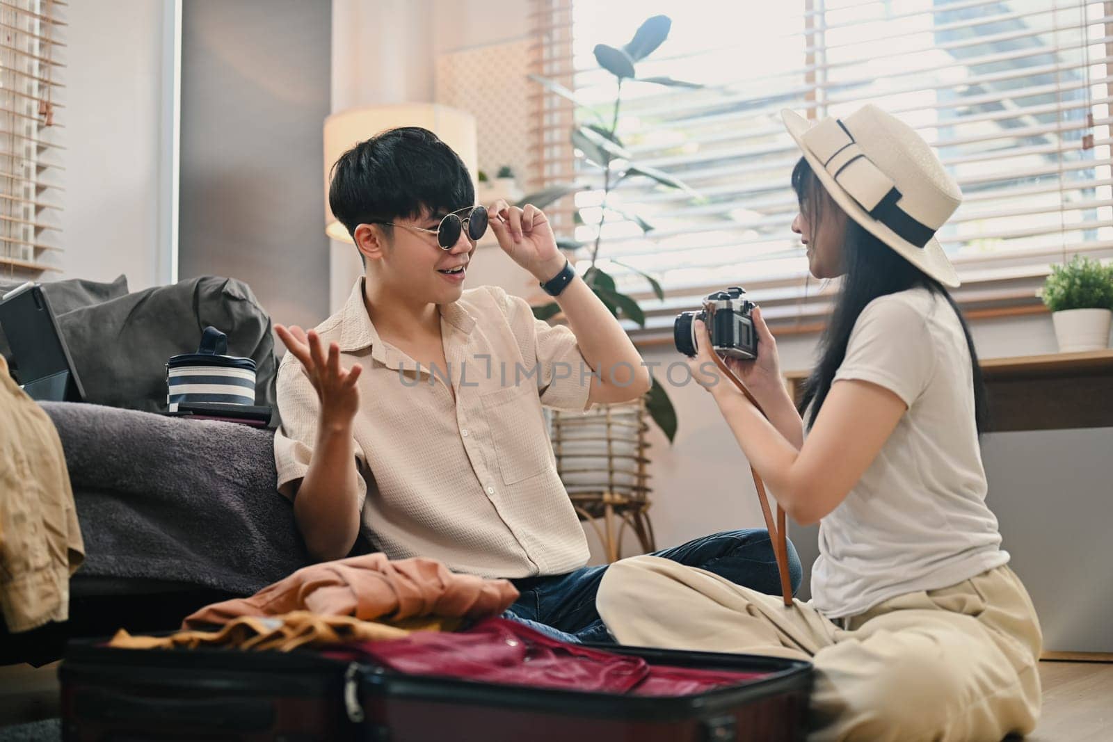 Happy Asian couple packing travel bag for summer vacation in living room. Traveling, vacation and lifestyle concept by prathanchorruangsak