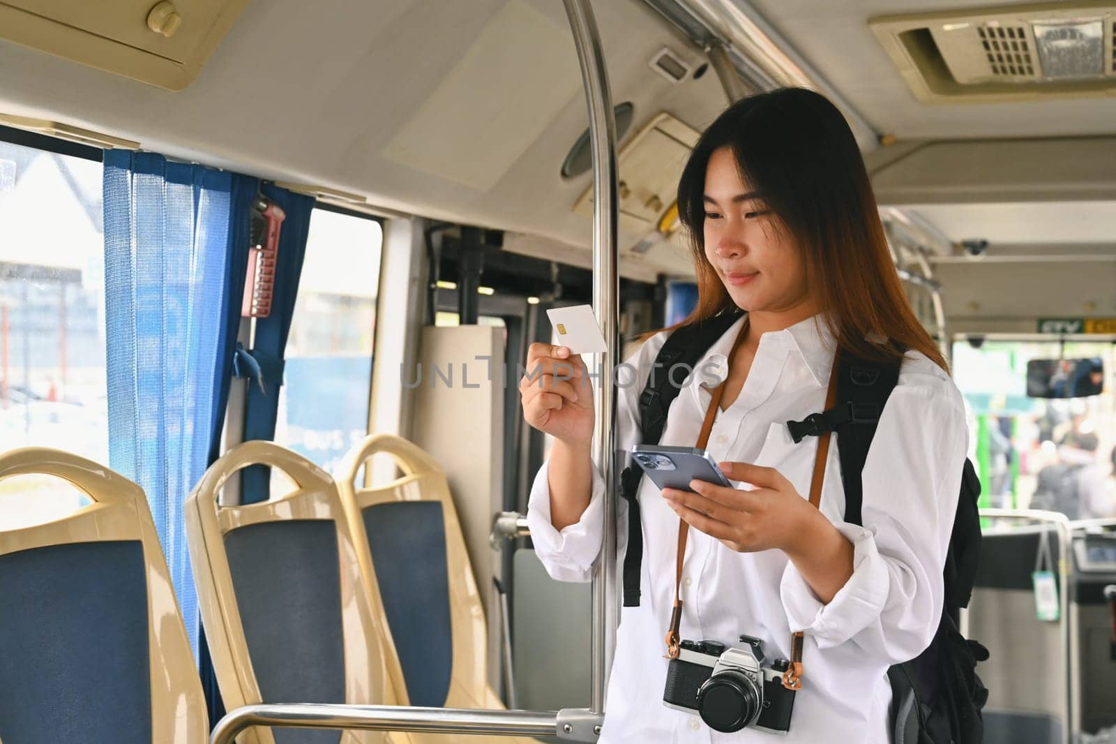 Young woman making mobile payment with credit card while standing in bus. Commuting and lifestyle concept.