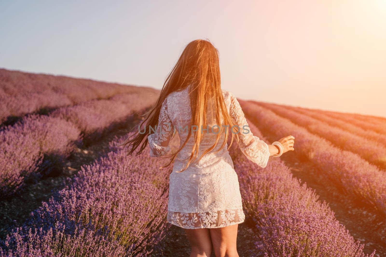 Close up portrait of young beautiful woman in a white dress and a hat is walking in the lavender field and smelling lavender bouquet.