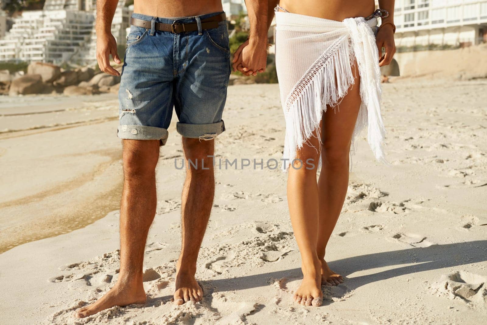 Love, holding hands and closeup of couple at a beach for walking, romance and bonding in nature together. Summer, zoom and legs or people at sea for travel, holiday or vacation with support or trust by YuriArcurs