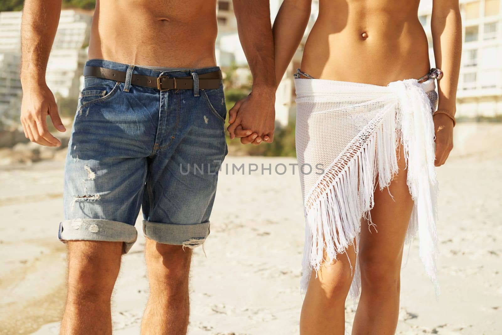Closeup, love and couple holding hands at a beach for walking, romance and bonding in nature together. Summer, zoom and legs or people at sea for travel, holiday or vacation with support or trust.