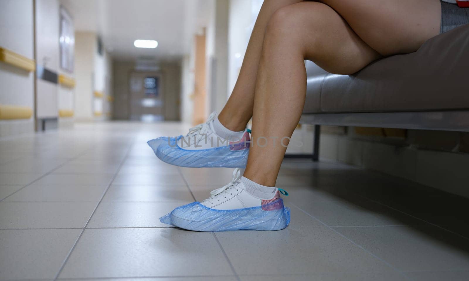 Woman in shoe covers sitting in hospital corridor closeup. Sanitary norms of behavior in medical institutions concept