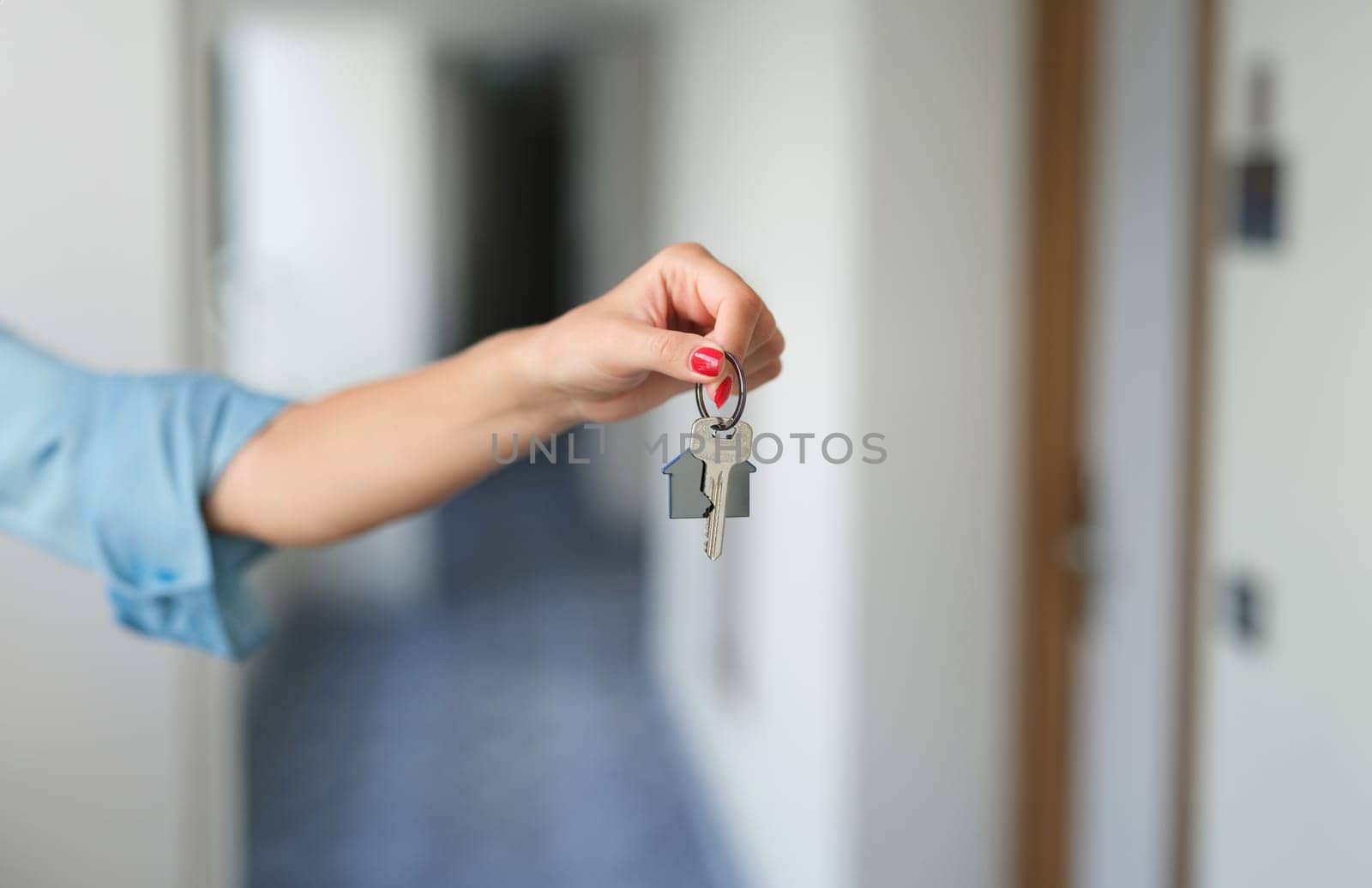 Female hand with red manicure holding house keys closeup. Buying property concept
