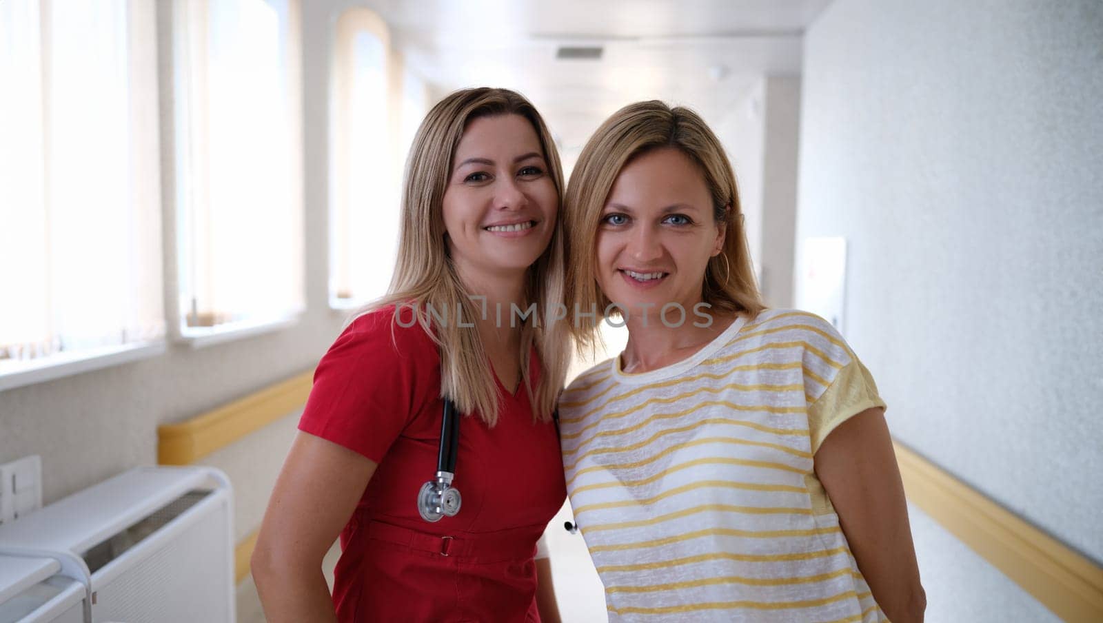 Portrait of young female doctor in red uniform and happy patient in clinic by kuprevich