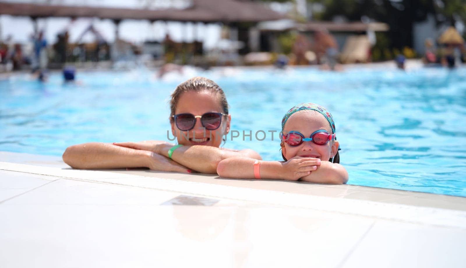 Little girl in swimming goggles and mother lying on side of pool by kuprevich