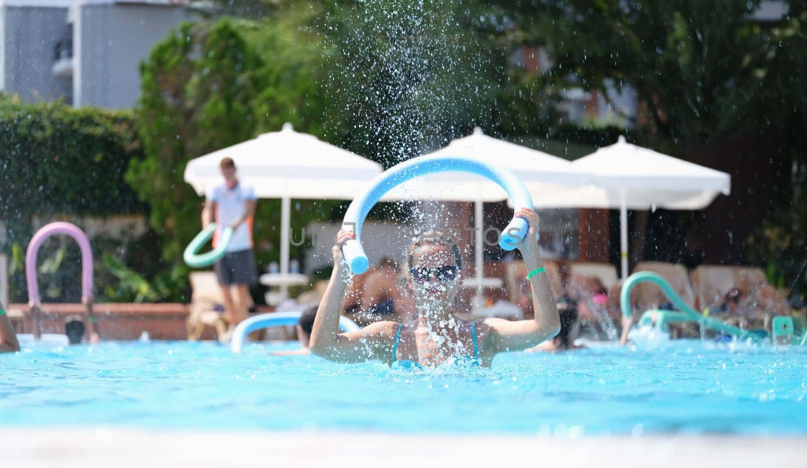 Young woman knocking noodle on water of swimming pool on aqua aerobics. Recreational sports concept