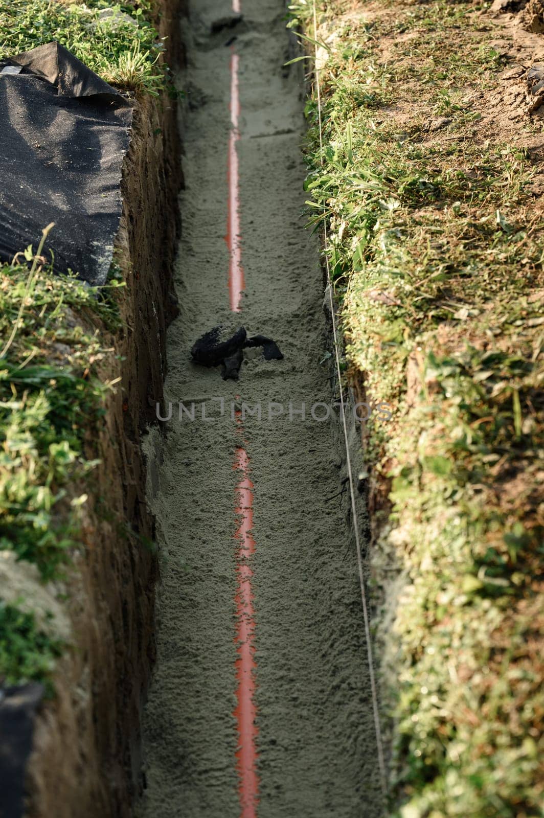 An orange reinforced sewer pipe is compacted with sand in a trench. Plumbing works on a private plot.