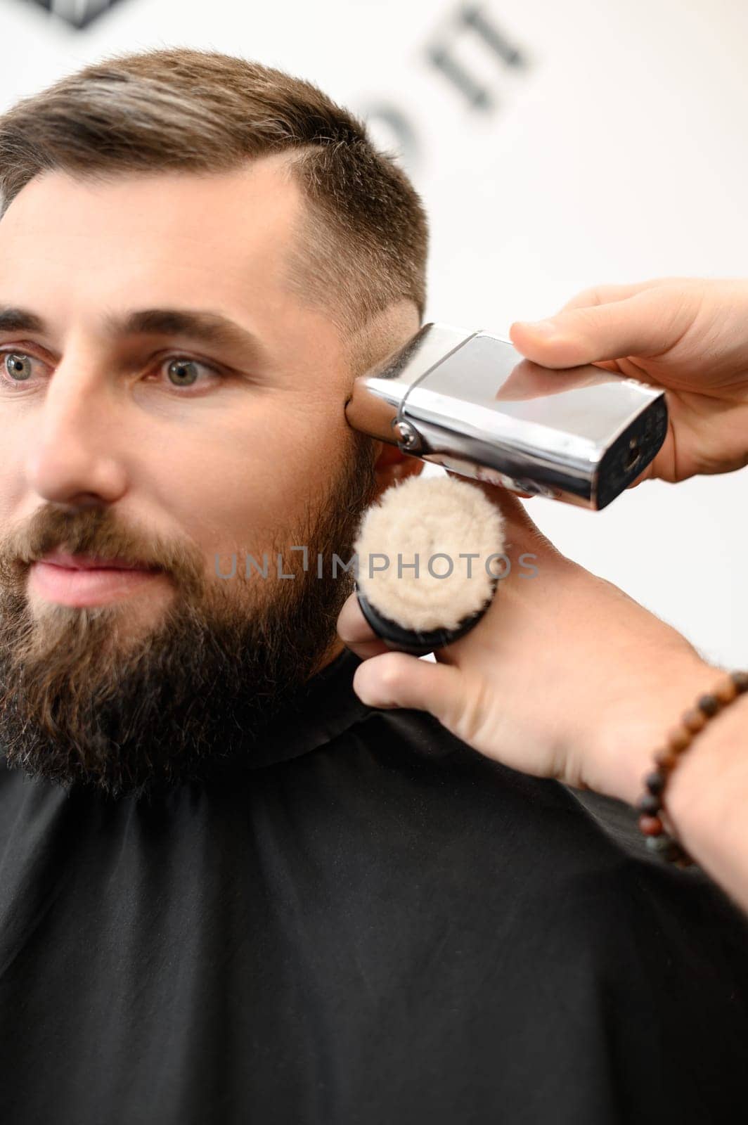 Barber shaves the temple with cordless trimmer during a short haircut on the sides of the head. by Niko_Cingaryuk