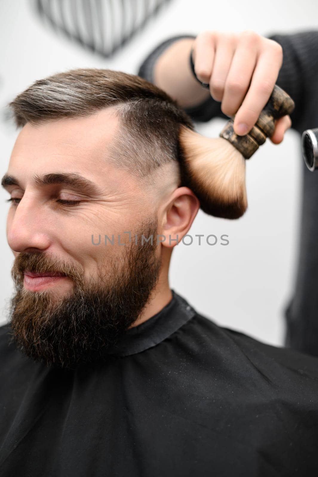 Barber sweeps hair with a brush while cutting a client hair in a salon. by Niko_Cingaryuk