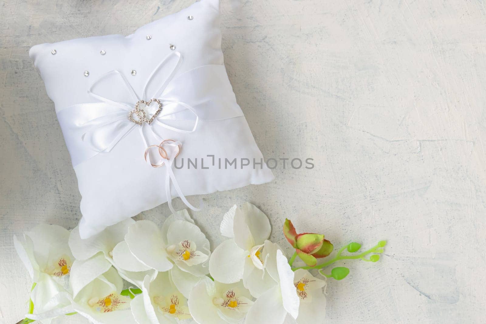 top view white orchid and wedding ring pillow on white textured background. gold rings on a ribbon. soft focus. flat lay . copy space