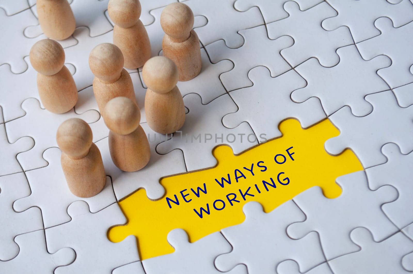 Empty jigsaw puzzle with text - new ways of working surrounded by wooden figures. Business culture.