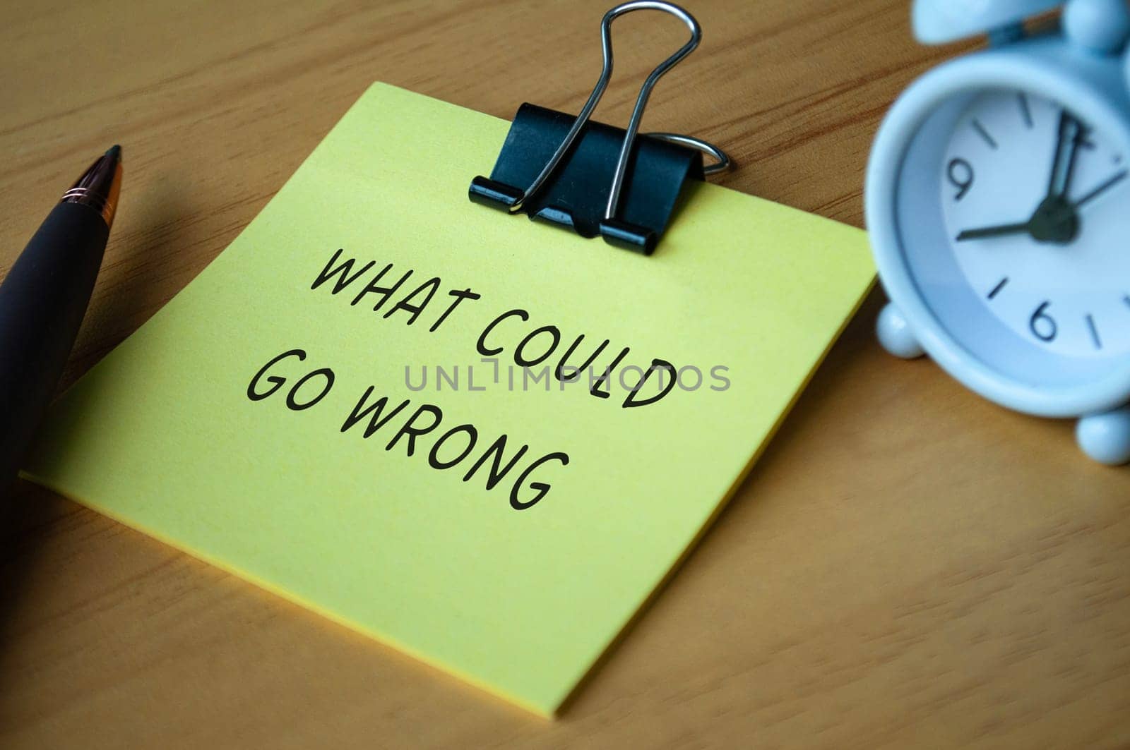 What could go wrong text on sticky note with alarm clock background.