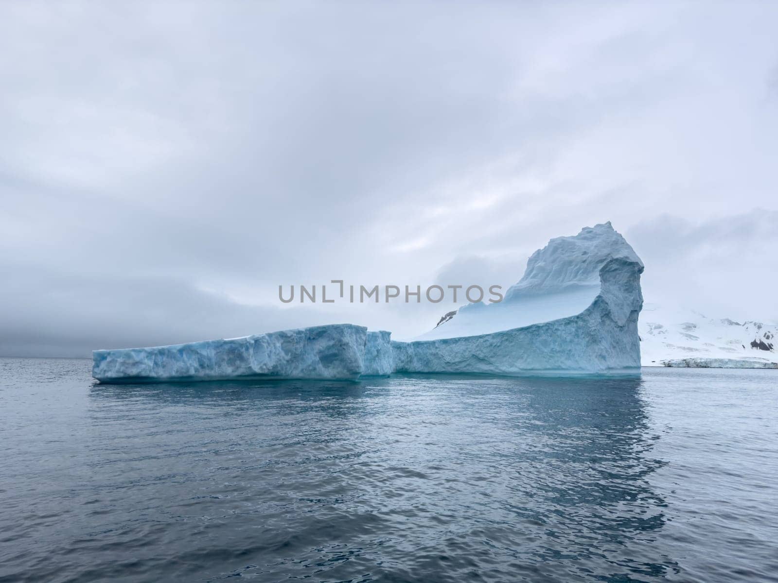 A huge high breakaway glacier drifts in the southern ocean off the coast of Antarctica at sunset, the Antarctic Peninsula, the Southern Arctic Circle, azure water, cloudy weather by vladimirdrozdin