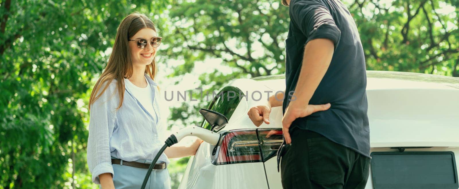 Focused EV car recharging electricity for battery on blurred couple. Exalt by biancoblue