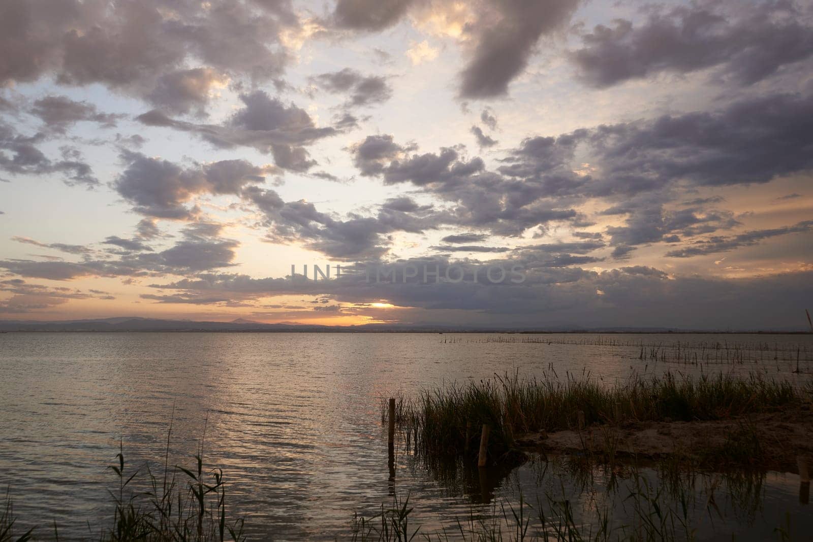 A sunset over the Valencia lagoon amidst the clouds.Reeds, reflections, calm waters, Mediterranean tradition and ecosystem,