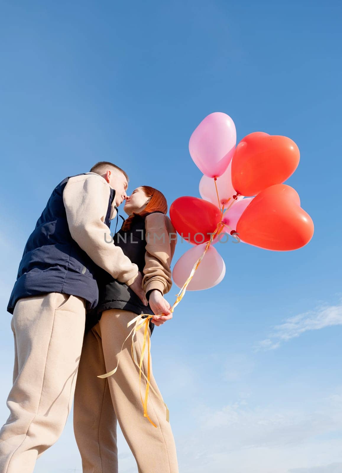 cheerful romantic couple dating and kissing outdoors with balloons by Desperada