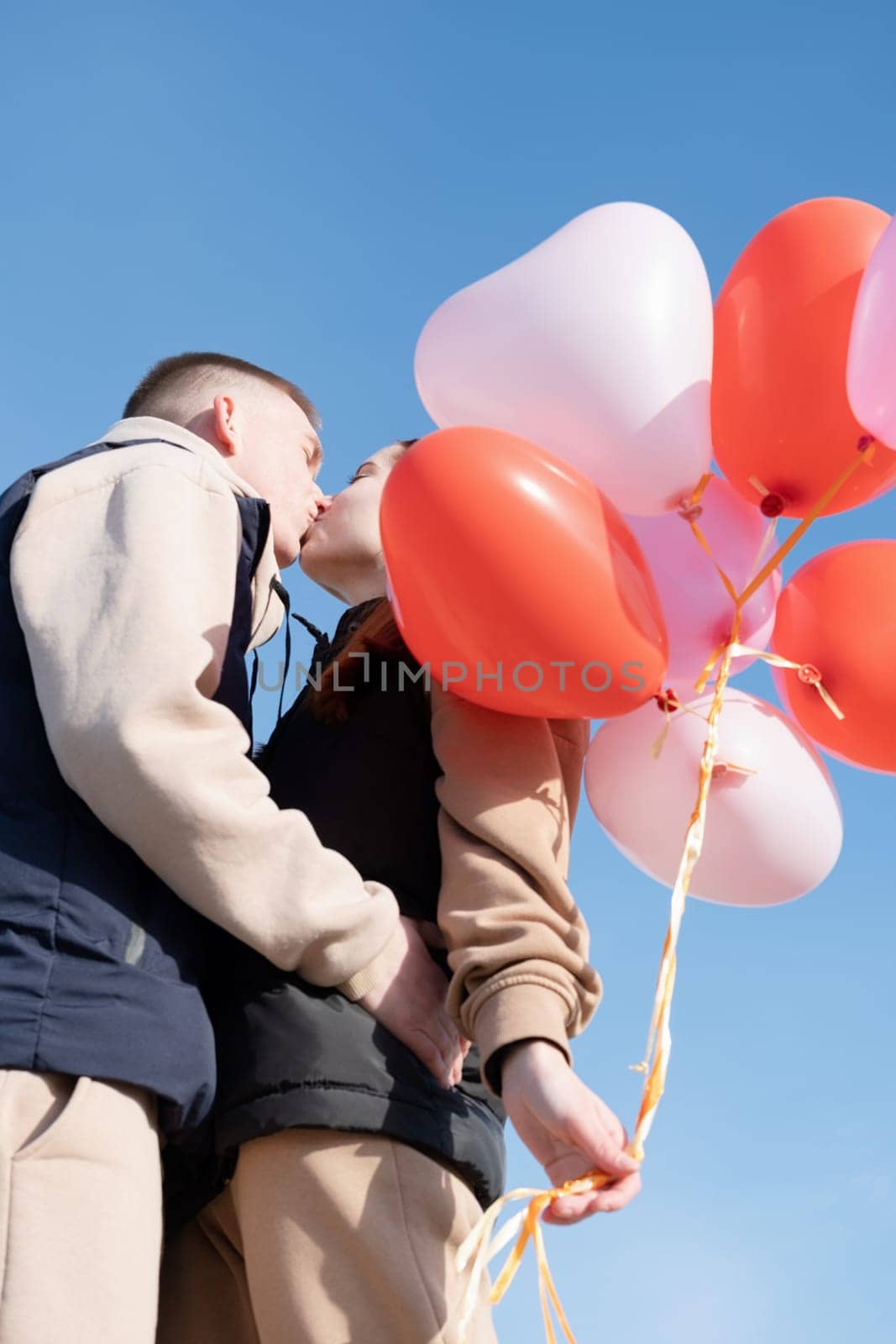 cheerful romantic couple dating and kissing outdoors with balloons by Desperada