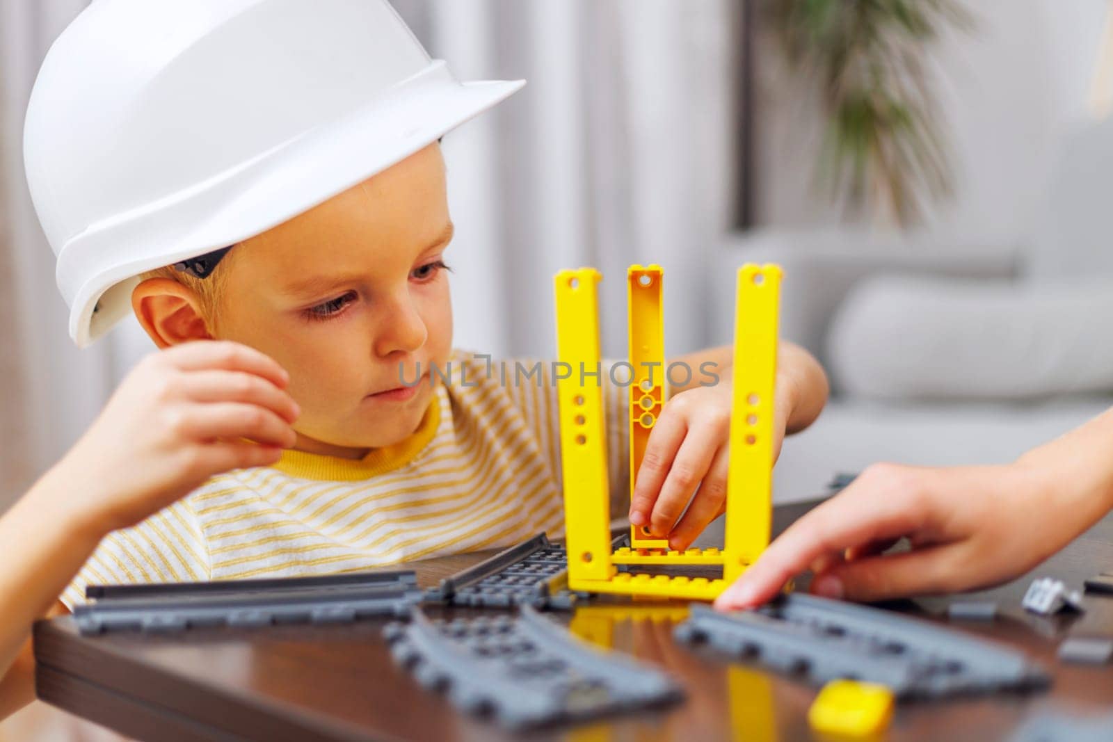 A focused child wearing a hard hat plays with a construction toy set indoors.