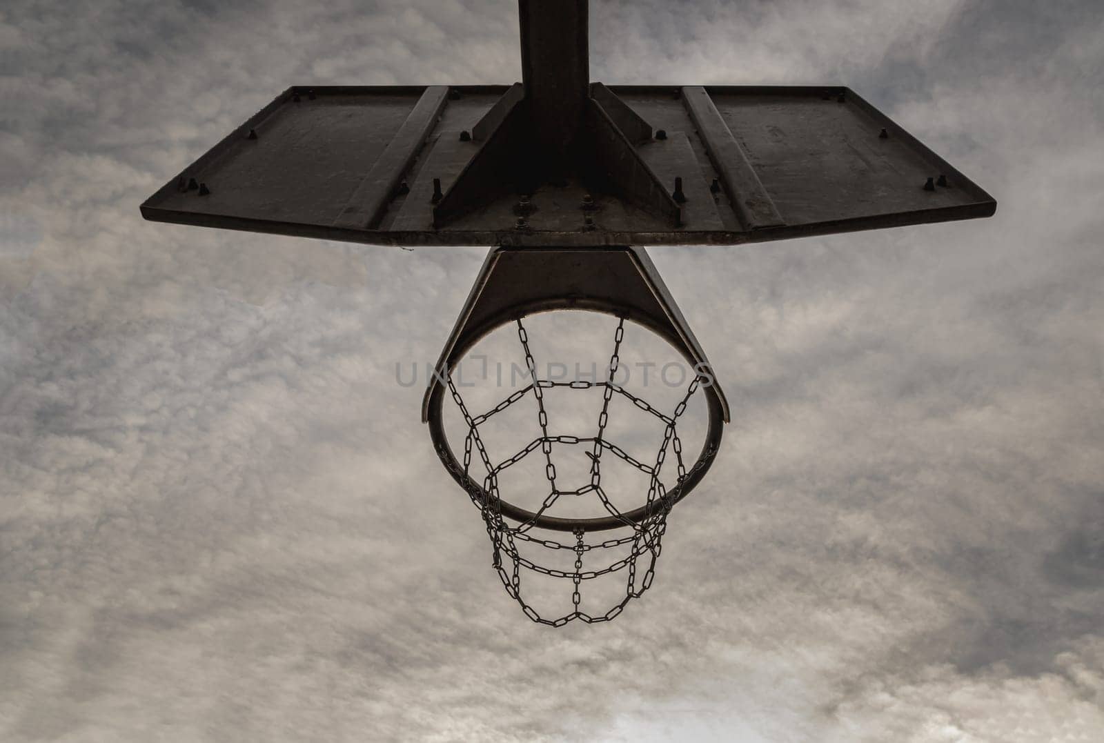 Edinburgh, Scotland, Jan 19, 2024 - Steel basketball backboard with the hoop metal ring and steel chain net against sky background seen from below. Street basketball court, Low angle view, Look up, Space for text, Selective focus.