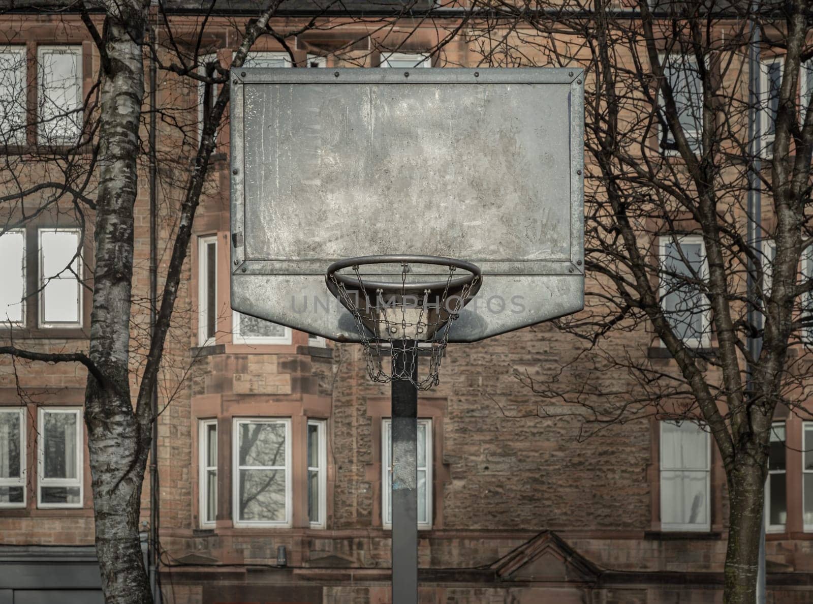 Edinburgh, Scotland, Jan 19, 2024 - Steel basketball backboard with the hoop metal ring and steel chain net at outdoor basketball courts with old buildings background in the city downtown. Space for text, Selective focus.