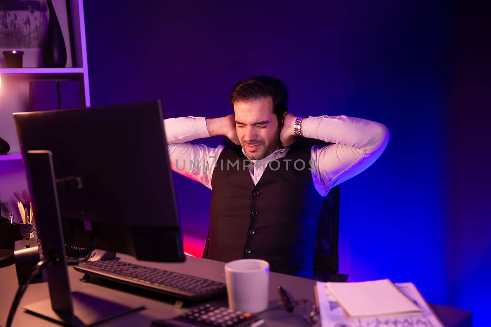 Smart businessman having aches with body in back, neck and whole body, stretching composition. Concept of market data analyzing long time at purple neon dark light room at late night time. Surmise.