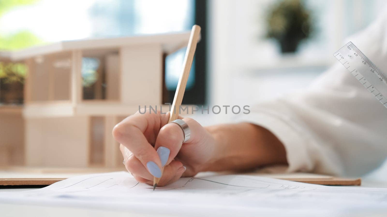 Closeup image of young beautiful caucasian architect engineer hand write mistake points on blueprint with house model placed on table at office. Creative and professional design concept. Immaculate.