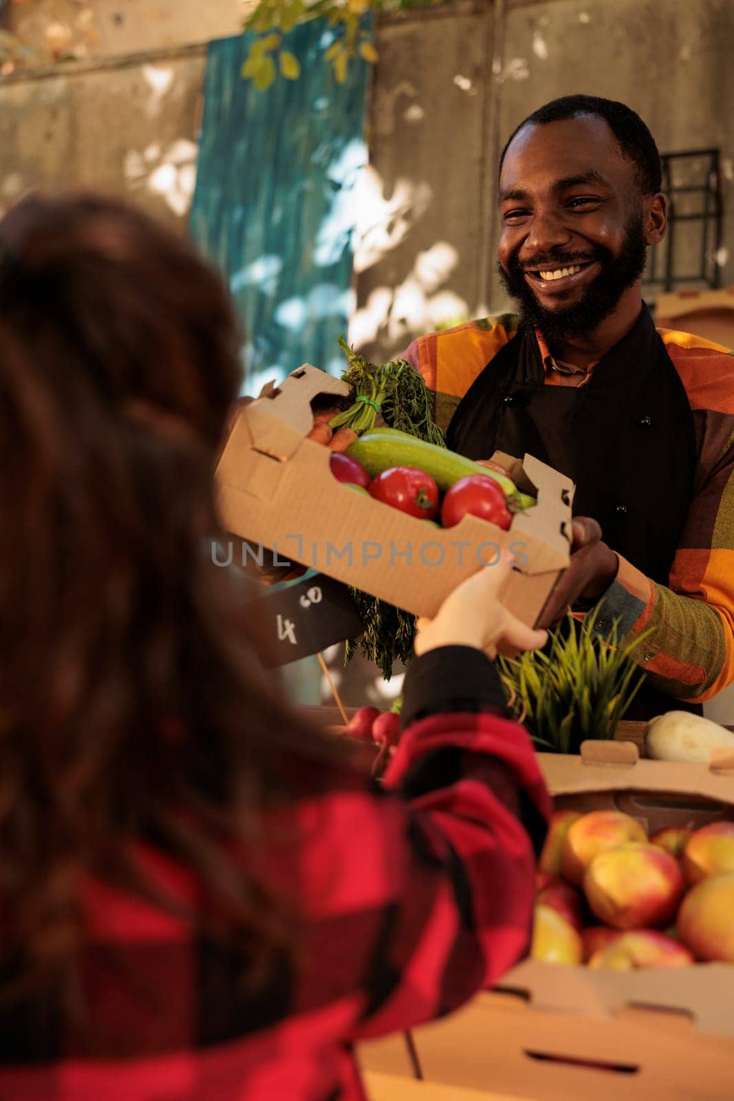 Male seller showing box of colorful farm products to woman by DCStudio