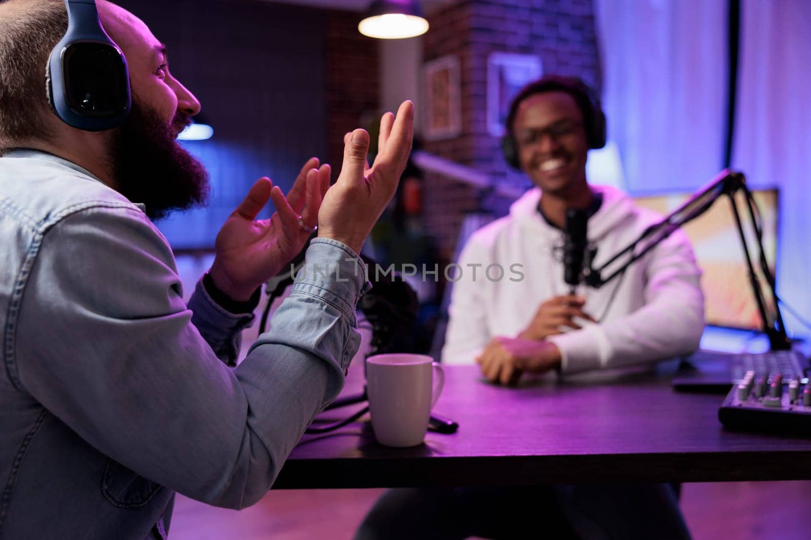 Online show host recording podcast with guest, telling jokes to eachother in home studio living room. Happy men having fun together during broadcasting session for internet streaming service
