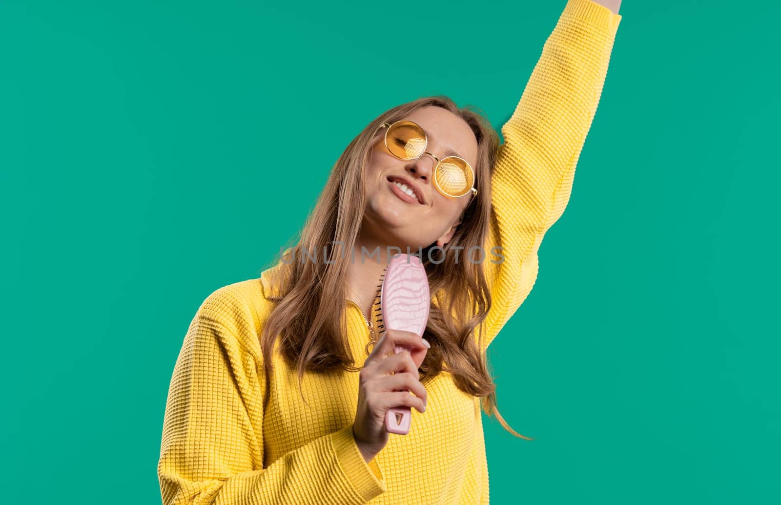 Woman singing, dancing with hair brush instead microphone on blue background. Lady having fun, listening to music, karaoke, dreams of being celebrity. High quality