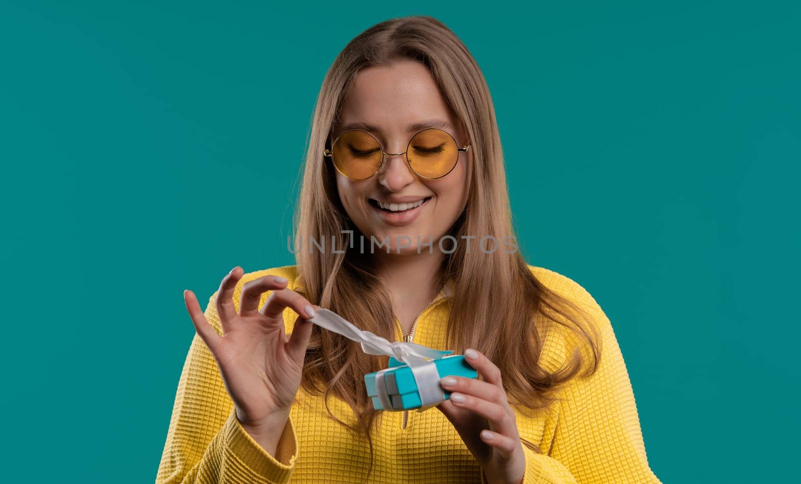 Happy woman gift box on blue background. Girl smiling, interested what's inside. Present, offer surprise for you. High quality photo