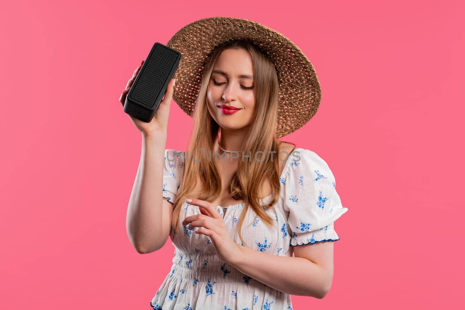 Woman dancing, enjoying on pink studio background. Girl moves to rhythm of music. Young teenager listening to music by wireless portable speaker - modern sound system. High quality