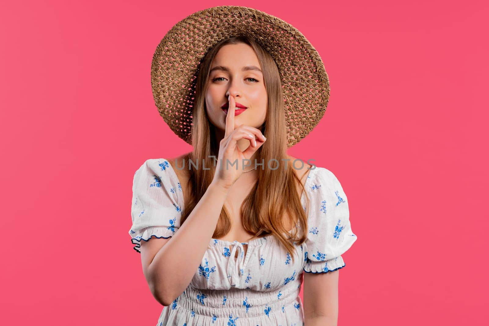 Smiling ukrainian woman holding finger on lips, pink studio background. Pretty lady with gesture of shhh, secret, silence, conspiracy, gossip concept. High quality